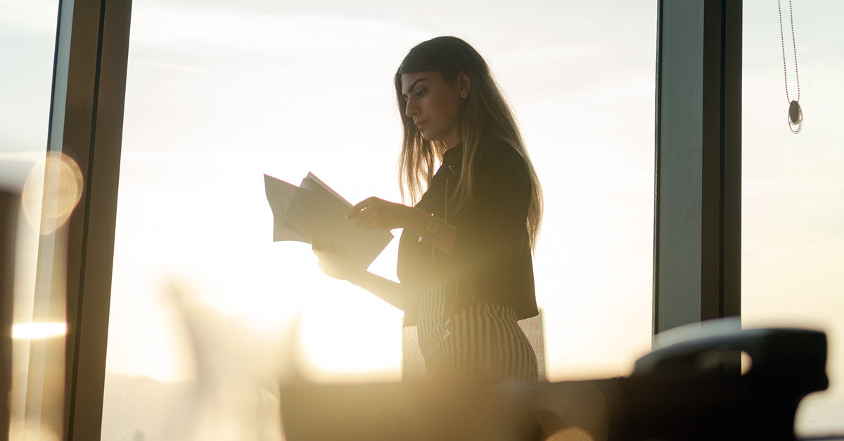 Business woman looking at papers in office with sunset in background