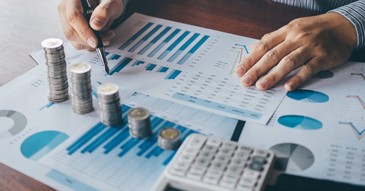 Analyzing financial data with charts, graphs, stacked coins, and a calculator on a table.