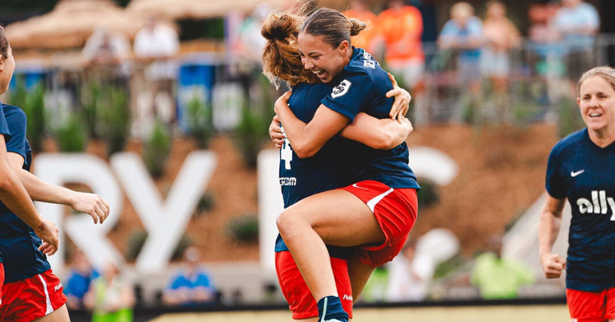Two female athletes hugging on the field.