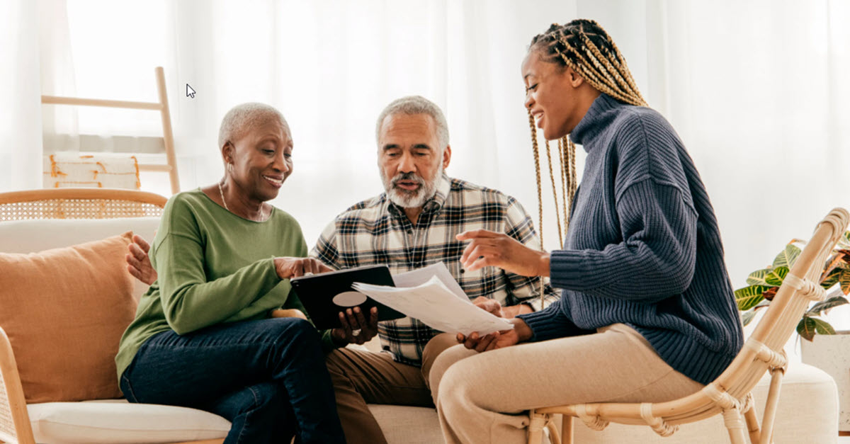 Older couple sitting with their daughter in their living room looking at accounts on a tablet and discussing finances.