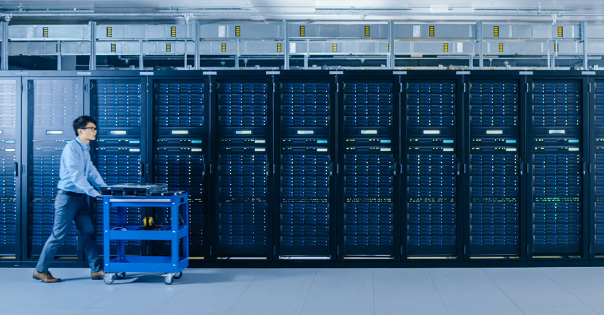 Employee pushes cart through servers in a data center.