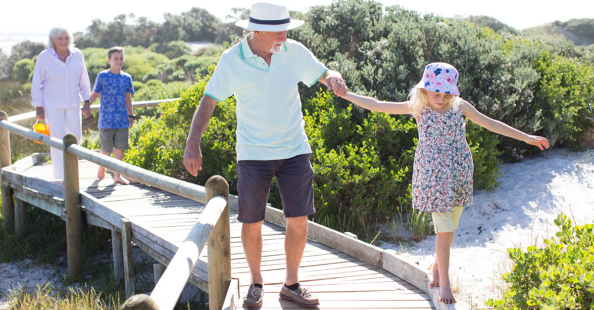 Grandparents holding their grandchildren's hands on a beach boardwalk.