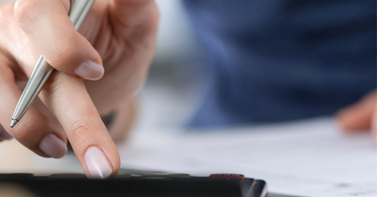 Hand holding a pen and typing in numbers into a calculator