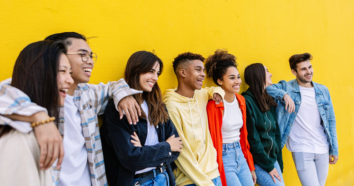 Group of young people leaning a against a yellow wall smiling