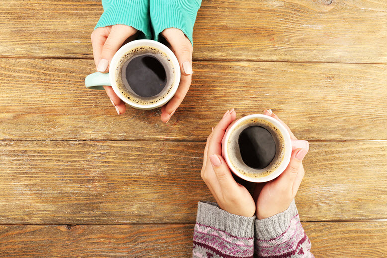 Two sets of hands, each cupping a mug of coffee on a table