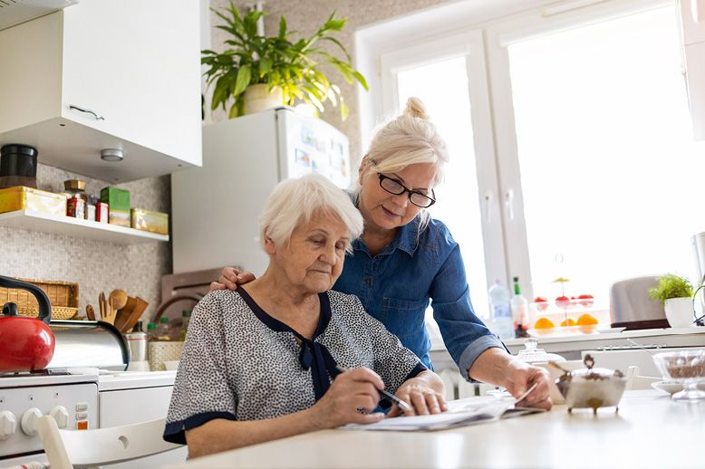 elderly-mother-and-adult-daughter-reviewing-paperwork-together-on-kitchen-counter-in-page