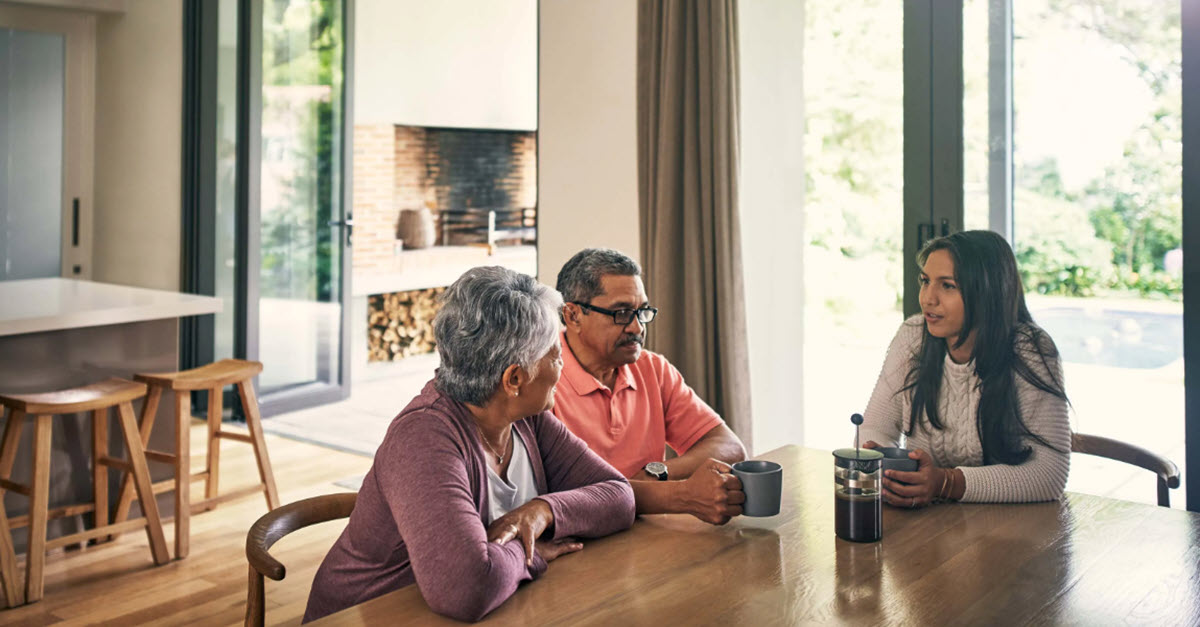 Older parents talking with their daughter around a dining table about finances