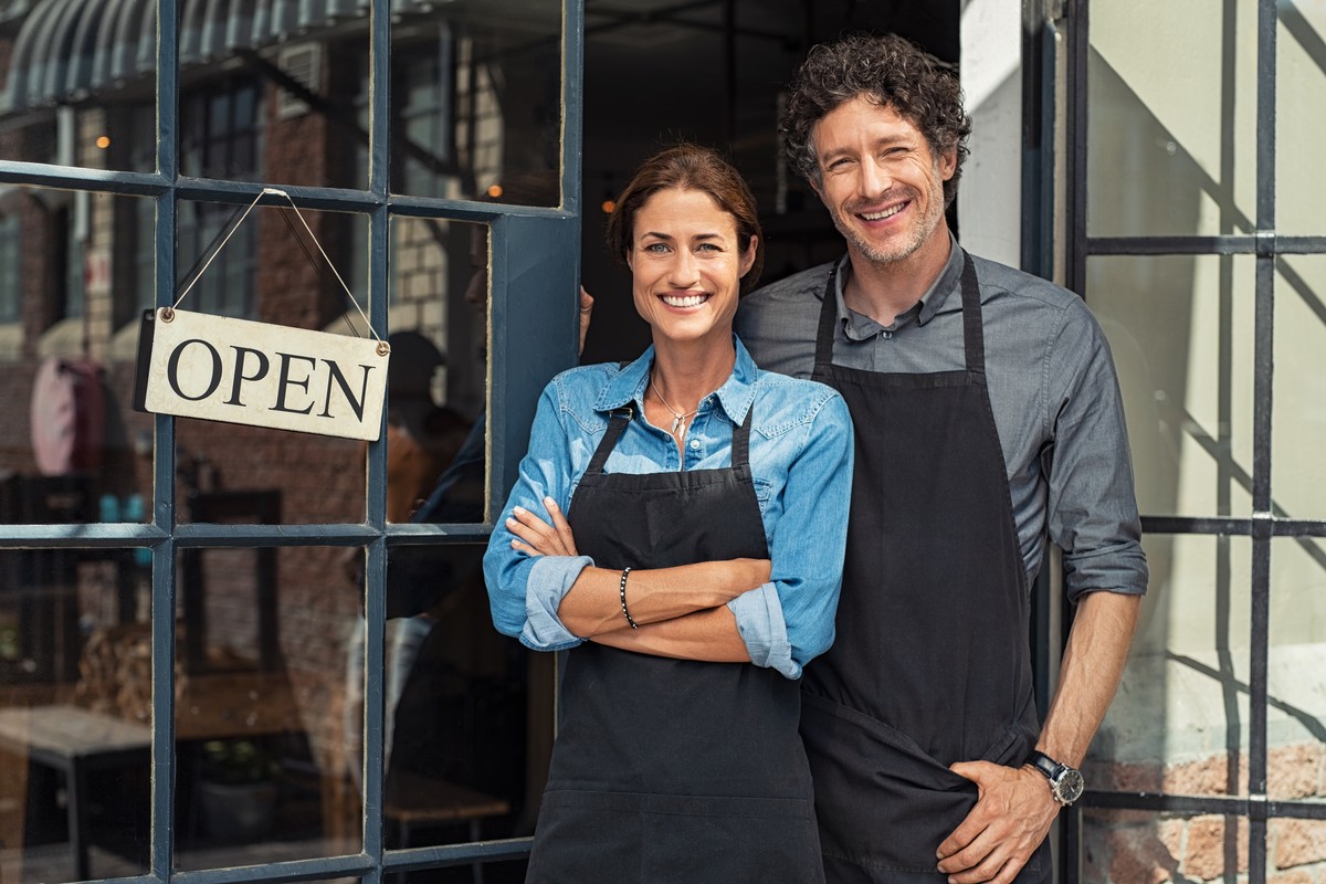 Restaurant owners posing in front of doors and open sign