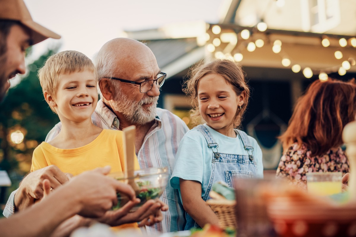 Grandfather sitting outdoors with granddaughter and grandson sitting on his lap